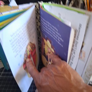 Pu&ograve; includere: Un libro fatto a mano con il dorso a motivi bianchi e neri, con pagine aperte che mostrano testo stampato e illustrazioni colorate di una persona con un cappello giallo. La pagina destra include il testo, Mammas Don't Let Your Babies Grow Up to Be Cowboys.