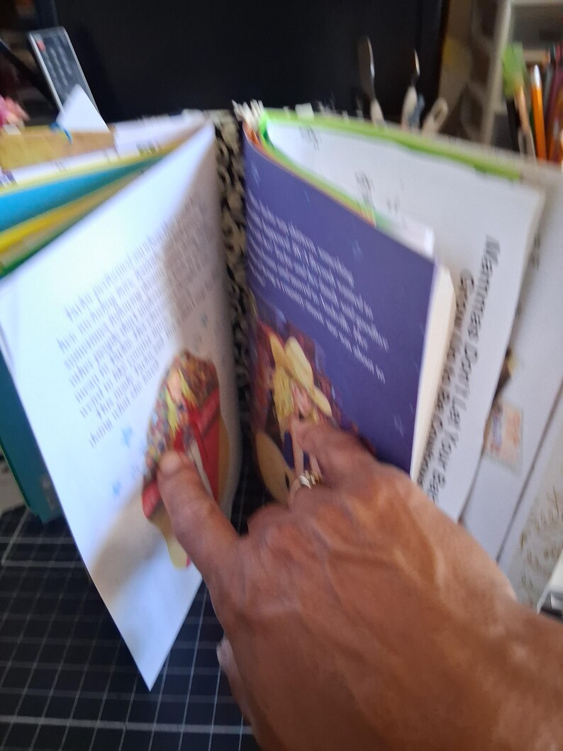 Pu&ograve; includere: Un libro fatto a mano con il dorso a motivi bianchi e neri, con pagine aperte che mostrano testo stampato e illustrazioni colorate di una persona con un cappello giallo. La pagina destra include il testo, Mammas Don't Let Your Babies Grow Up to Be Cowboys.