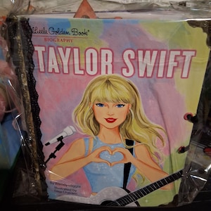 Pu&ograve; includere: Una biografia Little Golden Book di Taylor Swift, con una copertina illustrata che mostra una figura bionda che forma un cuore con le mani, un microfono e una chitarra. Il libro &egrave; avvolto in plastica trasparente con un bordo in pizzo nero.