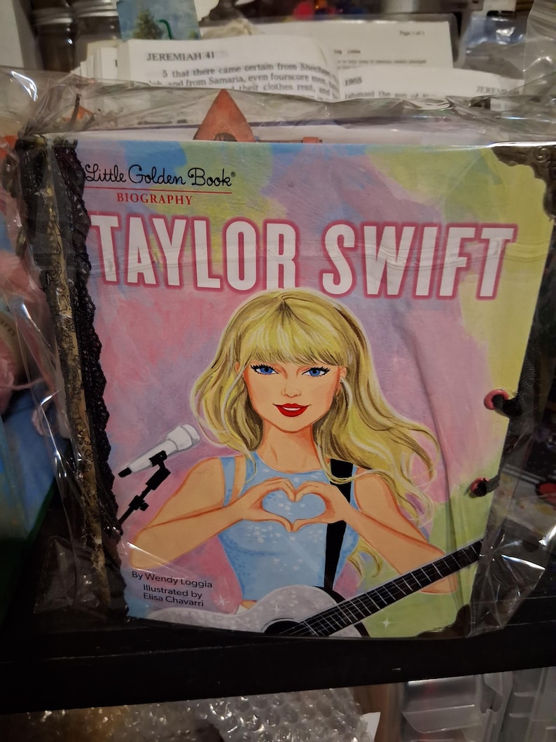 Pu&ograve; includere: Una biografia Little Golden Book di Taylor Swift, con una copertina illustrata che mostra una figura bionda che forma un cuore con le mani, un microfono e una chitarra. Il libro &egrave; avvolto in plastica trasparente con un bordo in pizzo nero.