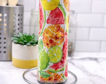 May include: A roll of reusable paper towels with a colorful fruit print. The print features watermelons, pineapples, limes, and green leaves on a white background. The roll is on a metal stand.