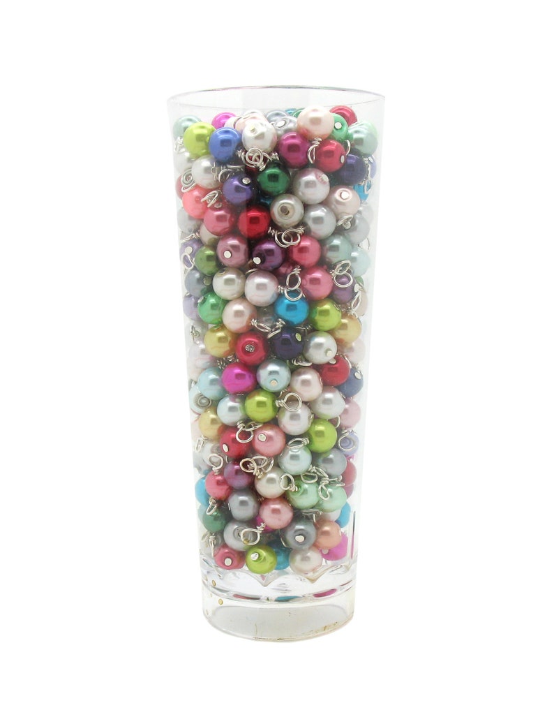 May include: A clear glass vase filled with a variety of colourful pearl beads. The beads are in shades of pink, blue, green, purple, and white.