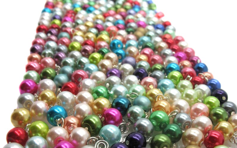 May include: A large assortment of colourful pearl beads, arranged in rows, with a variety of colours including pink, blue, green, and white.