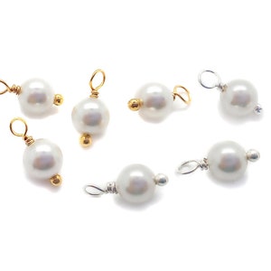 May include: Eight white pearl charms with gold and silver wire loops. The pearls are round and smooth.