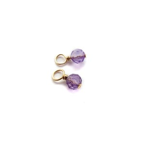 May include: Two gold-toned charms with a purple amethyst gemstone. Each charm has a small loop for attaching to a necklace or bracelet.
