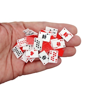 May include: A collection of miniature playing cards, featuring red and white designs. The cards display various suits and numbers, including hearts, spades, diamonds, and clubs. The cards are held in a hand.