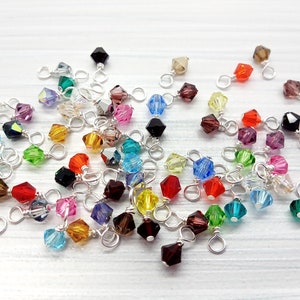 May include: Assortment of colorful crystal beads with silver wire loops. The beads are in various shapes and sizes, including round, square, and teardrop.