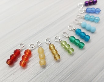May include: A rainbow of colours in a set of 10 bead charms. Each charm features three beads on a silver wire loop. The colours are red, orange, yellow, green, blue, light blue, turquoise, purple, and white.
