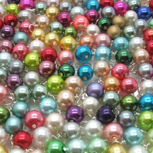 May include: A large assortment of colourful pearl beads with silver wire loops. The beads are arranged in a random pattern and are a mix of pastel and bright colours.