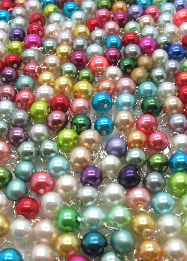 May include: A large assortment of colourful pearl beads with silver wire loops. The beads are arranged in a random pattern and are a mix of pastel and bright colours.
