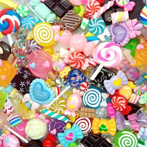 May include: A collection of colourful candy-themed charms featuring various shapes including lollipops, chocolate bars, wrapped hard candies, and swirls. The assortment includes pink, blue, yellow, and brown pieces with glossy finishes and small metal loops.