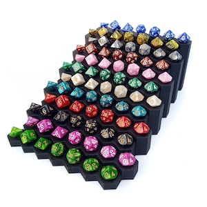 May include: A collection of colorful polyhedral dice displayed on a black hexagonal tiered stand. The dice are in various colors, including red, green, blue, pink, and yellow, with white or gold numbering. The stand is made of a dark material.