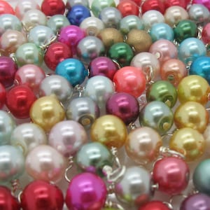 May include: A large assortment of colourful pearl beads in various shades of pink, blue, green, and white. The beads are arranged in a random pattern and are all approximately the same size.