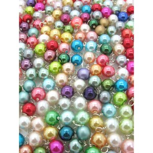 May include: A large assortment of colourful pearl beads, each with a silver wire loop. The beads are arranged in a random pattern, creating a visually appealing display.