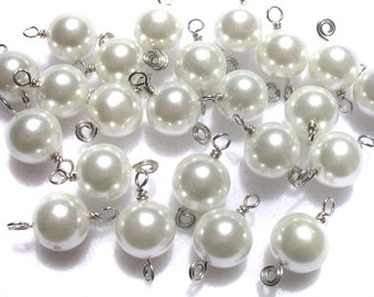 May include: A group of white pearl beads with silver wire loops. The beads are arranged in a random pattern on a white surface.