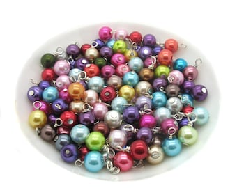 May include: A bowl filled with colourful pearl beads with silver wire loops. The beads are in various shades of pink, purple, green, blue, red, and brown.