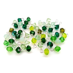 May include: A collection of green, light green, and clear glass beads with silver wire loops. The beads are faceted and have a variety of shapes.