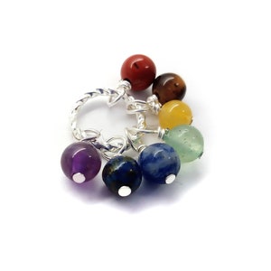 May include: A silver charm bracelet with seven colorful gemstone beads. The beads are red, brown, yellow, green, blue, and purple. The bracelet is made of twisted silver wire.