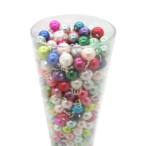 May include: A clear glass container filled with a variety of colourful pearl beads. The beads are in shades of pink, green, blue, purple, and white.