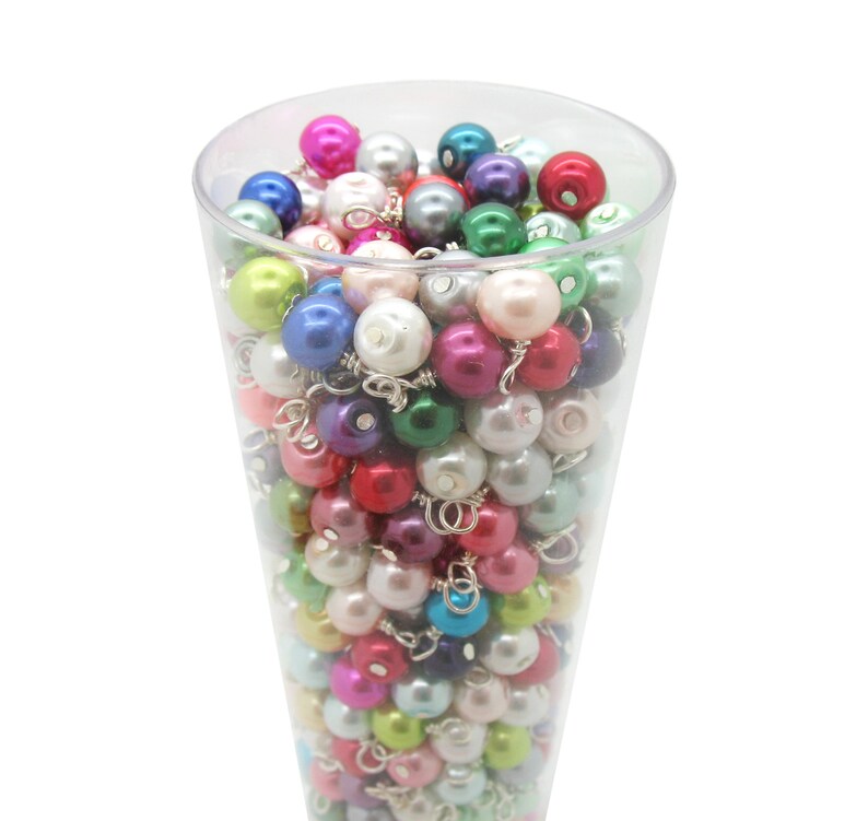 May include: A clear glass container filled with a variety of colourful pearl beads. The beads are in shades of pink, green, blue, purple, and white.