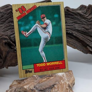 May include: A baseball card featuring Todd Worrell of the St. Louis Cardinals. The card has a wooden-like border with the text "'86 Record Breaker." The bottom of the card reads "Most Saves, Season, Rookie."