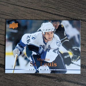 May include: A hockey trading card featuring Martin St. Louis of the Tampa Bay Lightning. The card shows St. Louis in his white and blue Lightning jersey, with the team logo on the front. The card has the Upper Deck logo in the upper left corner.