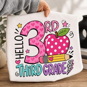 Könnte beinhalten: Ein weißes T-Shirt mit einem Grafikdesign und dem Text Hello 3rd Third Grade. Das Design zeigt eine große rosa Zahl Drei mit Herzmuster, einen rosa Apfel mit weißen Punkten, einen gelben Bleistift und einen Blitz mit Leopardenmuster.