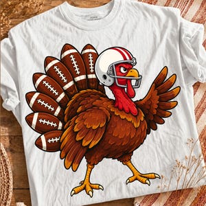 May include: A white t-shirt featuring a graphic of a brown turkey wearing a white football helmet with red stripes. The turkey's tail feathers are shaped like brown footballs with white laces. The turkey has a red wattle and an angry expression.