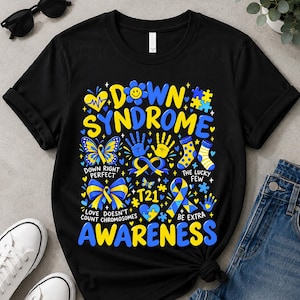 Peut inclure: Un t-shirt noir avec un motif graphique coloré portant les inscriptions Down Syndrome Awareness, T21, Down Right Perfect, The Lucky Few et Love Doesn't Count Chromosomes, orné de cœurs, papillons, rubans et chaussettes bleus et jaunes.