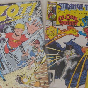 May include: Two comic book covers side-by-side. The left cover features a red, yellow, and blue superhero character flying through the air with a gun in his hand. The right cover features a blue and purple superhero character with a white cape and a yellow and white superhero character with a white cape. The text on the right cover reads "Strange Tales Featuring Cloak & Dagger & Doctor Strange".