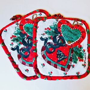 May include: Set of three red and white pot holders with a Christmas theme. The pot holders feature a green heart with the text "From the Heart" and a green and red holly design.