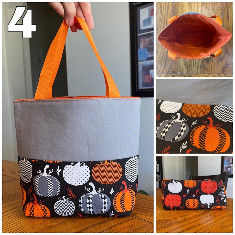 May include: A gray and orange tote bag with a pumpkin pattern. The bag has two orange handles and a gray lining. The bag is sitting on a wooden surface.