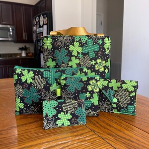 May include: Four different sized bags with a black background and green shamrock pattern. The largest bag has a gold handle.