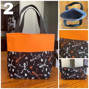 May include: A black and orange Halloween trick-or-treat bag with a skeleton and skull pattern. The bag has two black handles and a solid orange top section.