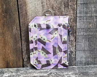 May include: A purple leather wallet with a zipper closure and a clear ID window. The wallet is covered in a repeating pattern of a popular character from the Star Wars franchise.