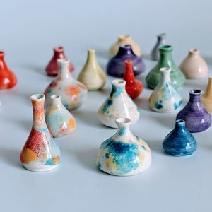 May include: A collection of small, colorful ceramic vases in various shapes and sizes. The vases are decorated with abstract patterns and splashes of color, including blue, green, red, yellow, and white.