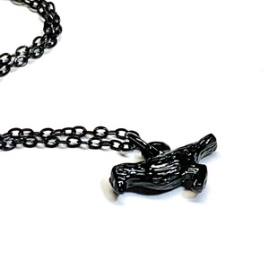 May include: A black chain necklace with a black bird pendant. The bird is in flight with its wings spread out.