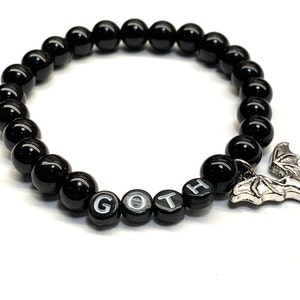 May include: Black beaded bracelet with a silver bat charm and the word "GOTH" spelled out in white letters on the beads.
