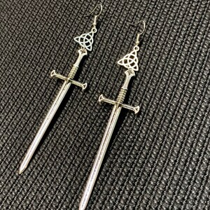 May include: A pair of silver earrings featuring a sword design with a Celtic knot at the top.