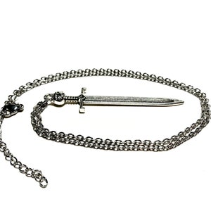 May include: A silver sword pendant necklace with a chain. The sword is detailed with a cross guard and a pointed tip.