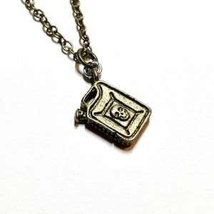 May include: A silver chain necklace with a gold-toned pendant shaped like a gas can with a skull and crossbones design.