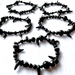 May include: Four black beaded bracelets with sharp, pointed accents. Each bracelet is made of black beads and has a unique design of pointed accents.