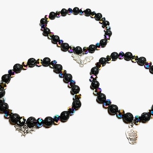 May include: Three black lava rock bracelets with iridescent crystal accents. One bracelet has a silver bat charm, and another has a silver skull charm.