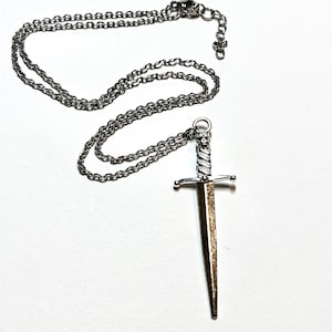 May include: A silver chain necklace with a silver dagger pendant. The dagger has a twisted handle and a pointed tip.