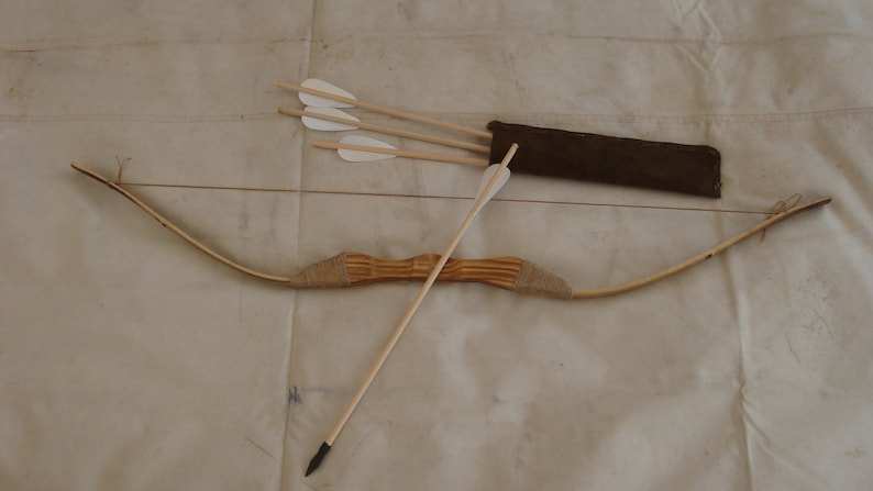 Op de afbeelding: Een houten boog en pijlset met een bruine koker. De boog is gemaakt van natuurlijk hout en heeft een bruine snaar. De pijlen zijn ook van hout en hebben witte veren.