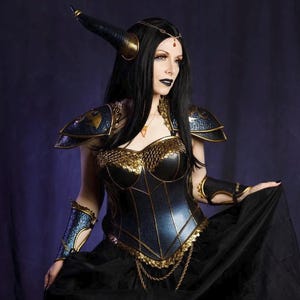 May include: A fantasy costume featuring a black and gold corset, shoulder armor, and arm cuffs. The costume includes a black skirt and a horned headpiece. The overall design has a medieval or gothic aesthetic.
