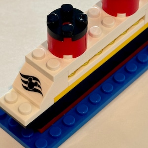 May include: A white and blue Lego ship with red and black smokestacks. The ship has a Mickey Mouse logo on the side.