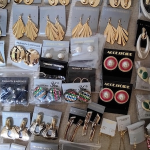 May include: A collection of various fashion earrings displayed on individual cards, including gold-toned metal shapes, pearl-like studs, colorful rhinestone circles, and dangling designs. Some pairs are packaged in clear plastic sleeves.
