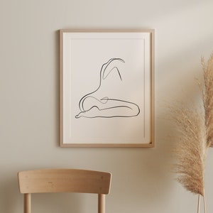 May include: A black and white line drawing of a person in a seated pose, printed on a white background and framed in a light wood frame.