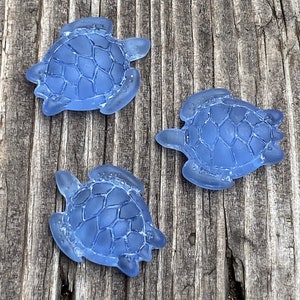 Puede incluir: Tres figuritas de tortuga marina de vidrio azul sobre una superficie de madera.